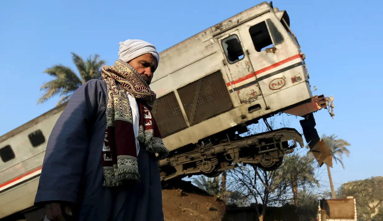 Warga saat berjalan disamping kereta api yang mengalami kecelakaan fatal di Beni Suef, Kairo , (11/2). Belum diketahui jelas korban akibat kecelakaan tersebut. (REUTERS / Mohamed Abd El Ghany)