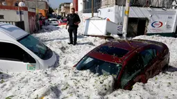 Seorang polisi berdiri di dekat kendaraan yang tertimbun salju di jalanan di wilayah timur Guadalajara, negara bagian Jalisco, Meksiko (30/6/2019). Salju yang turun di kota itu cukup tebal, bahkan di beberapa tempat mencapai 1,5 meter. (AFP Photo/Ulises Ruiz)