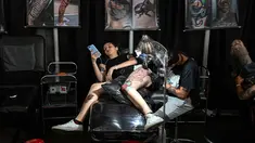 Seorang wanita bermain ponsel saat membuat tato dikakinya selama Expotattoo Colombia 2019 di Medellin, departemen Antioquia (2/6/2019). Para penggila tato antusias untuk mentato tubuhnya di festival tato terbesar di negara tersebut. (AFP Photo/Joaquim Sarmiento)