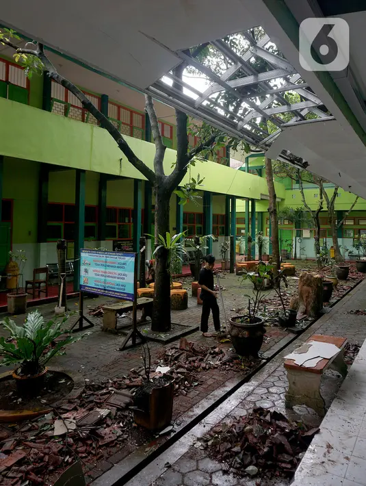 Pekerja membersihkan reruntuhan genting yang memenuhi halaman sekolah akibat gempa di SMK Negeri 1 Turen, Malang, Jawa Timur, Minggu (11/4/2021). Gempa yang mengguncang kawasan Malang dan sekitarnya membuat sejumlah bangunan rusak. (merdeka.com/Nanda F. Ibrahim)