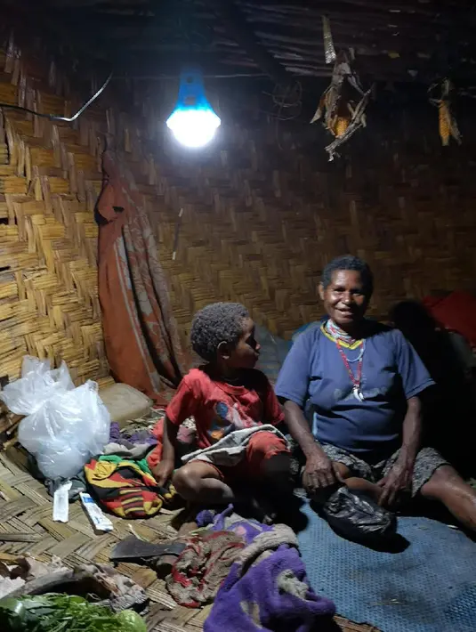 Seorang ibu dan anaknya duduk di bawah Lampu Tenaga Surya Hemat Energi (LTSHE) di Distrik Puldama, Kabupaten Yahukimo, Provinsi Papua. LTSHE bisa dinyalakan secara manual lewat tombol di lampu atau dengan remote control. (Liputan6.com/HO/Hadi M Juraid)