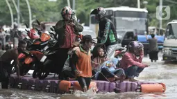 Pengendara sepeda motor menggunakan jasa rakit saat banjir melanda Cempaka Putih, Jakarta, Minggu (23/2/2020). Pengendara memanfaatkan jasa angkutan rakit yang ditawarkan warga agar dapat melewati banjir. (merdeka.com/Iqbal S. Nugroho)