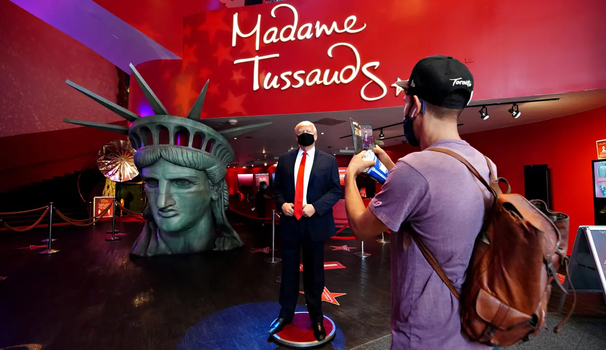 Pengunjung menganbil foto sosok Donald Trump yang bermasker saat Madame Tussauds New York dibuka kembali di New York City, Kamis (27/8/2020). Patung lilin Donald Trump akan berada di pintu masuk untuk mengingatkan tentang protokol kesehatan, termasuk pemakaian masker (Cindy Ord/Getty Images/AFP)