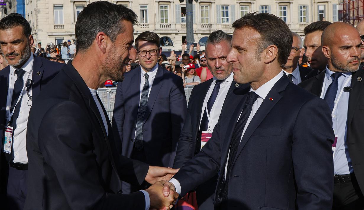 Presiden Prancis, Emanuel Macron (kanan) berjabat tangan dengan Presiden Komite Penyelenggara Olimpiade dan Paralimpiade Paris 2024 (Cojo) Tony Estanguet saat upacara penyambutan kedatangan api Olimpiade dan Paralimpiade Paris 2024 di Vieux-Port (Pelabuhan Tua) Marseille, Pranci, Rabu (08/05/2024) waktu setempat. (AFP/Pool/Ludovic Marin)
