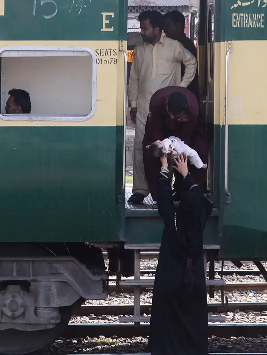 Seorang wanita menyerahkan anaknya kepada pria sebelum naik kereta untuk melakukan perjalanan pulang untuk merayakan Idul Fitri di sebuah stasiun kereta api di Lahore (2/6/2019). Muslim di seluruh dunia bersiap untuk merayakan Idul Fitri yang menandai akhir bulan puasa Ramadan. (AFP Photo/Arif Ali)