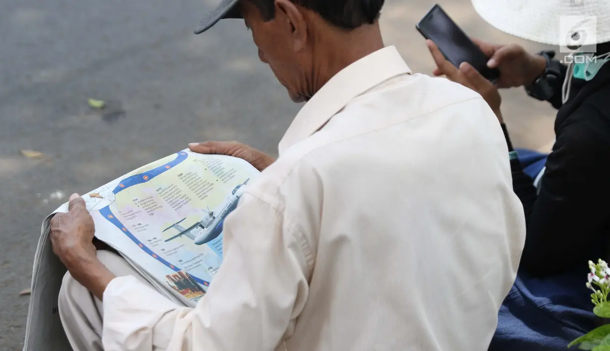Warga membaca koran sambil menunggu di sisi jalan TMP Kalibata untuk melihat prosesi pemakaman Presiden RI ke-3 BJ Habibie, Jakarta, Kamis (12/9/2019). BJ Habibie meninggal pada Rabu (11/9/2019) pukul 18.05 WIB di usia 83 tahun. (Liputan6.com/Helmi Fithriansyah)