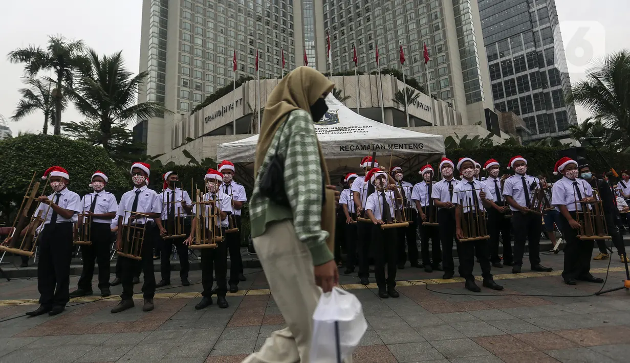 Seorang wanita berjalan di depan para peserta yang sedang bermain angklung saat acara Christmas in Jakarta di Bundaran Hotel Indonesia, Jakarta, Selasa (21/12/2021). Pemerintah Provinsi DKI Jakarta menggelar Christmas in Jakarta dalam rangka menyambut Natal 2021. (Liputan6.com/Johan Tallo)