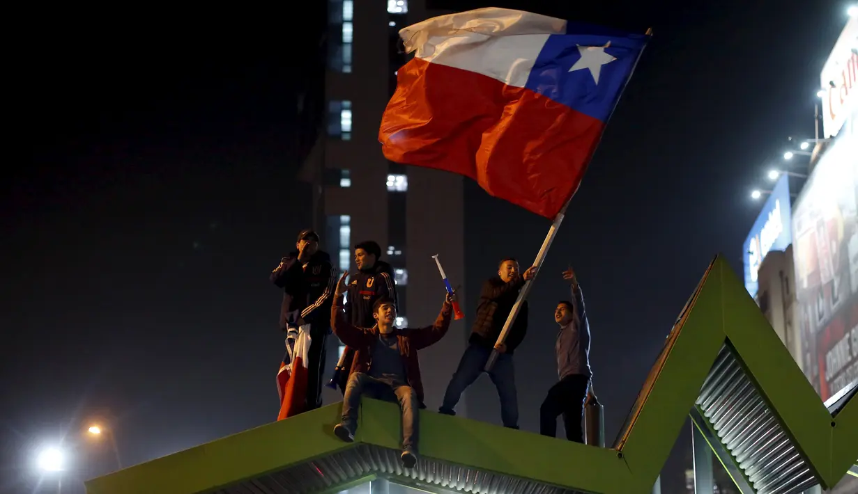 Sejumlah Suporter berada diatas atap mengibarkan bendera nasional Chile merayakan kemenangan Chile atas Uruguay di Copa America 2015 di Santiago, Chile, (25/6/2015). Chile melaju ke semifinal usai mengalahkan Uruguay 1-0. (REUTERS/Pablo Sanhueza)