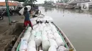 Pekerja mengangkut barang menggunakan perahu menuju dermaga di Desa Pantai Mekar, Muaragembong, Kabupaten Bekasi, Senin (6/12/2021). Jasa angkut barang menggunakan perahu tersebut banyak diminati warga untuk mempersingkat waktu perjalanan. (Liputan6.com/Herman Zakharia)