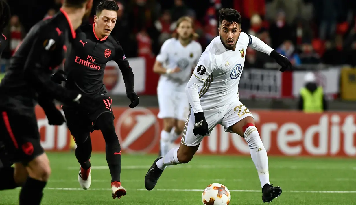 Pemain Arsenal Mesut Ozil berebut bola dengan pemain Ostersunds Brwa Nouri pada laga leg pertama babak 32 besar Liga Europa di Jamtkraft Arena, Jumat (16/2). Arsenal memetik kemenangan tandang 3-0 atas Ostersunds. (Robert Henriksson/TT News Agency via AP)