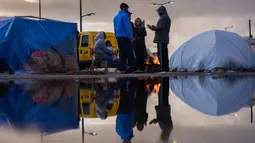 Israel mengklaim tindakan ini sebagai respons atas serangan dari kelompok Hizbullah. Tampak dalam foto, para pengungsi menghangatkan diri di sekitar api unggun di luar tenda mereka di sepanjang kawasan tepi laut Beirut, Lebanon, pada Senin 30 Maret 2026. (Dimitar DILKOFF/AFP)