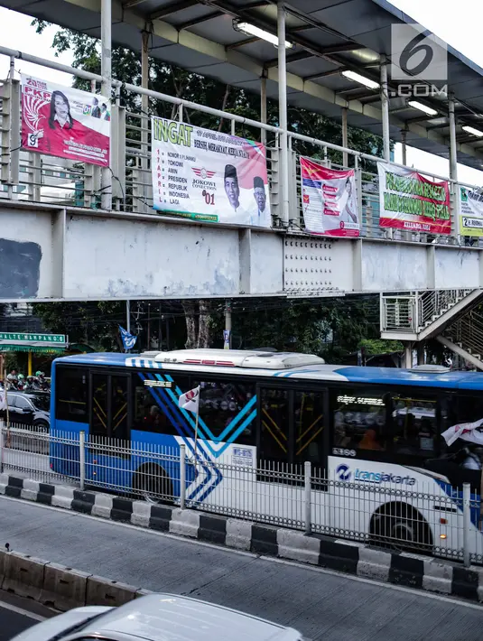 Transjakarta melintas di bawah Jembatan Penyeberangan Orang (JPO) yang dipasangi alat peraga kampanye (APK) di Mampang, Jakarta, Rabu (27/2). Meski sudah dilarang, namun masih ditemukan pemasangan APK di tempat terlarang. (Liputan6.com/Faizal Fanani)