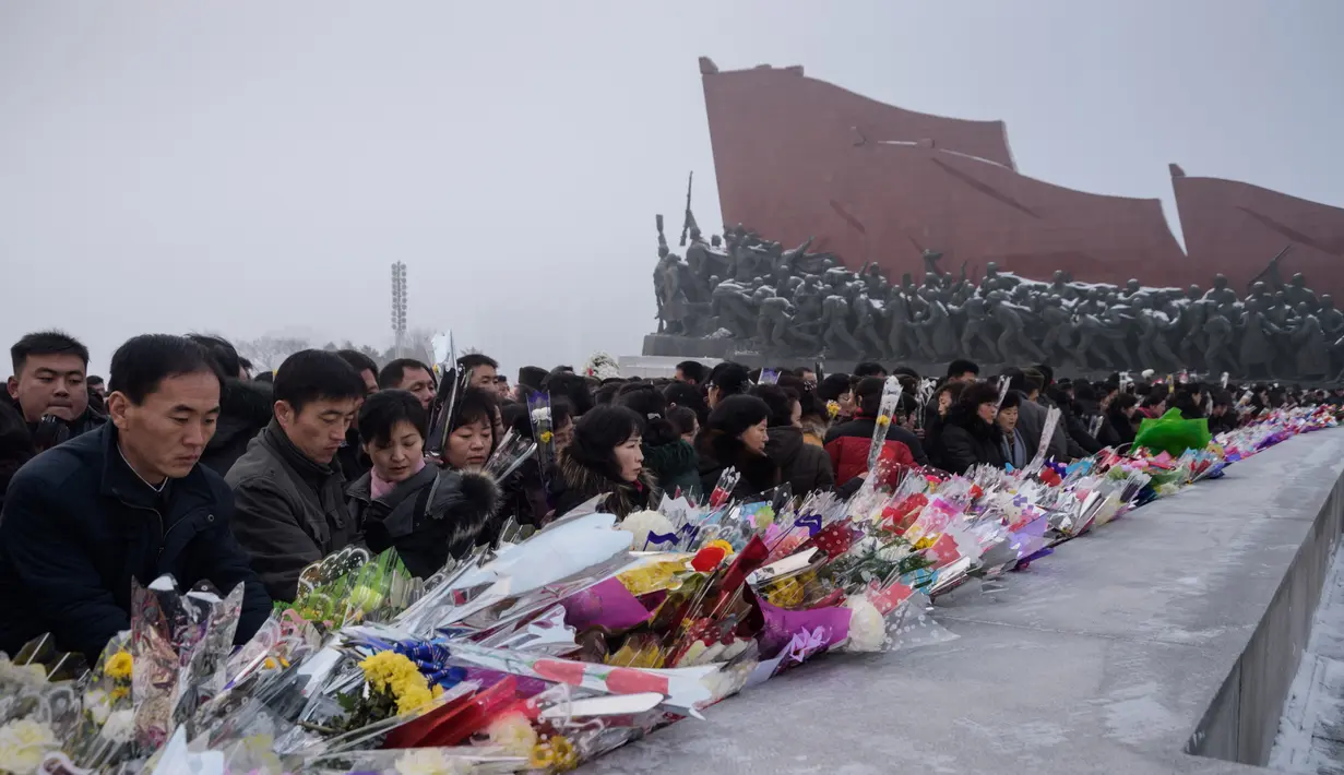 Penduduk Pyongyang meletakkan bunga di depan patung pemimpin Korea Utara Kim Il Sung dan Kim Jong Il selama Hari Peringatan Nasional di Bukit Mansu, Pyongyang (17/12).  Korea Utara tengah memperingati 7 tahun wafatnya  Kim Jong Il. (AFP Photo/Kim Won Jin)