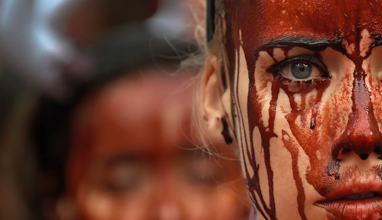 Aktivis membasahi wajahnya dengan darah palsu saat aksi menolak festival San Fermin di Pamplona, Spanyol, (5/7). Festival yang menampilkan tradisi lari bersama banteng dan matador ini merupakan aksi yang mengorbankan hewan. (REUTERS/Susana Vera)