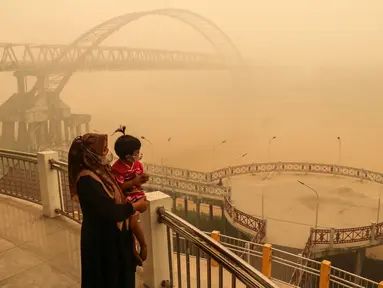 Seorang ibu bersama anaknya yang mengenakan masker melihat kondisi sekitar dari atas jembatan di tengah kabut asap tebal akibat kebakaran hutan dan lahan di Palangkaraya, Kalimantan Tengah, Senin (12/10/2026). Kabut asap menyelimuti sejumlah wilayah di Indonesia, Malaysia, dan Singapura selama beberapa pekan terakhir akibat kebakaran yang melanda kawasan hutan di Kalimantan dan Sumatra. Asap dari kebakaran tersebut terbawa angin hingga melintasi wilayah regional dan berdampak pada kualitas udara. (Reina/AFP)