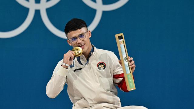 Peraih medali emas dari Indonesia, Rizki Juniansyah, berpose di podium setelah pertandingan angkat besi kelas -73kg putra selama Olimpiade Paris 2024 di South Paris Arena di Paris, pada 8 Agustus 2024. (Miguel MEDINA/AFP)
