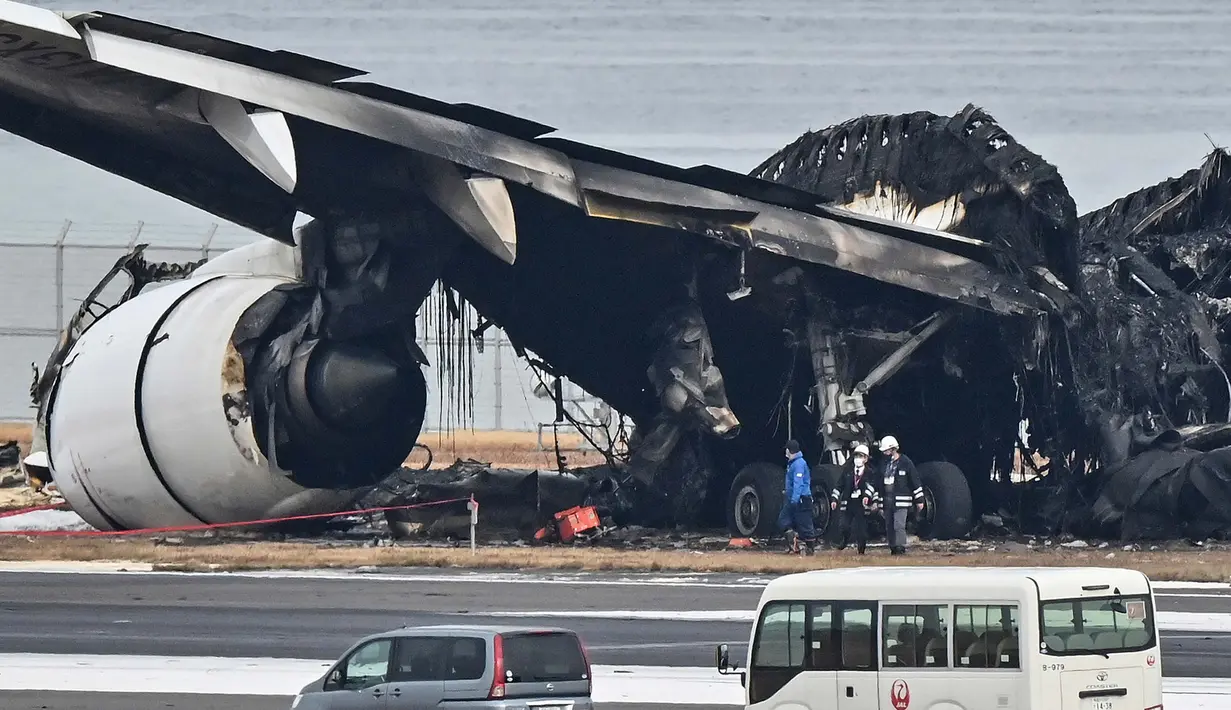 Para petugas melihat puing-puing pesawat penumpang Japan Airlines (JAL) yang terbakar di landasan pacu di Bandara Internasional Tokyo di Haneda di Tokyo pada tanggal 3 Januari 2024. (Richard A. Brooks/AFP)