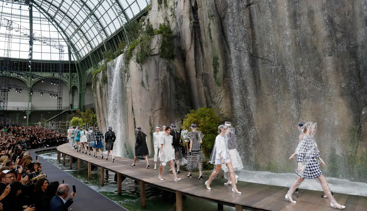 Para model berjalan di catwalk menampilkan koleksi Spring/Summer 2018 untuk Chanel selama Paris Fashion Week, Selasa (3/10). Lengkap dengan air terjun di dalam gedung, model berjalan memakai peralatan musim hujan yang ultra-chic. (Patrick KOVARIK / AFP)