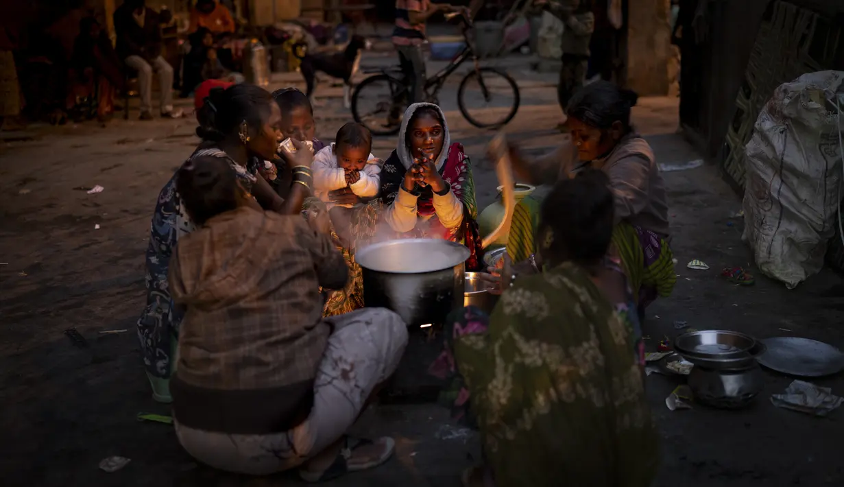 Sebuah keluarga tunawisma berkumpul di sekitar kompor pada malam yang dingin di kompleks tempat penampungan bobrok untuk para tunawisma di New Delhi, Jumat, 30 Desember 2022.  Banyak tempat penampungan malam penuh sesak, dengan toilet yang tidak bersih. Kamar bau busuk. Dan terkadang tidak ada air. (AP Photo/Altaf Qadri)