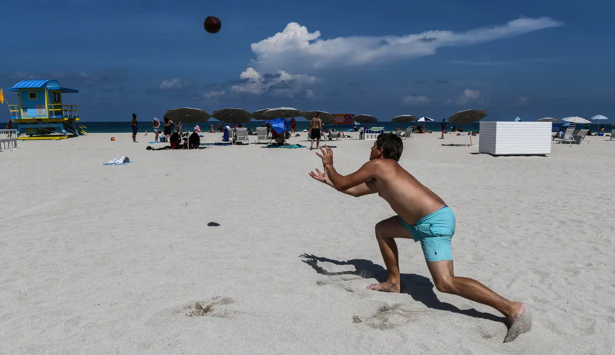 Pengunjung bermain bola di Miami Beach di Florida, Rabu (10/6/2020). Pantai Miami dibuka hari ini untuk pertama kalinya setelah hampir tiga bulan ditutup guna menekan jumlah penyebaran corona Covid-19. (CHANDAN KHANNA / AFP)