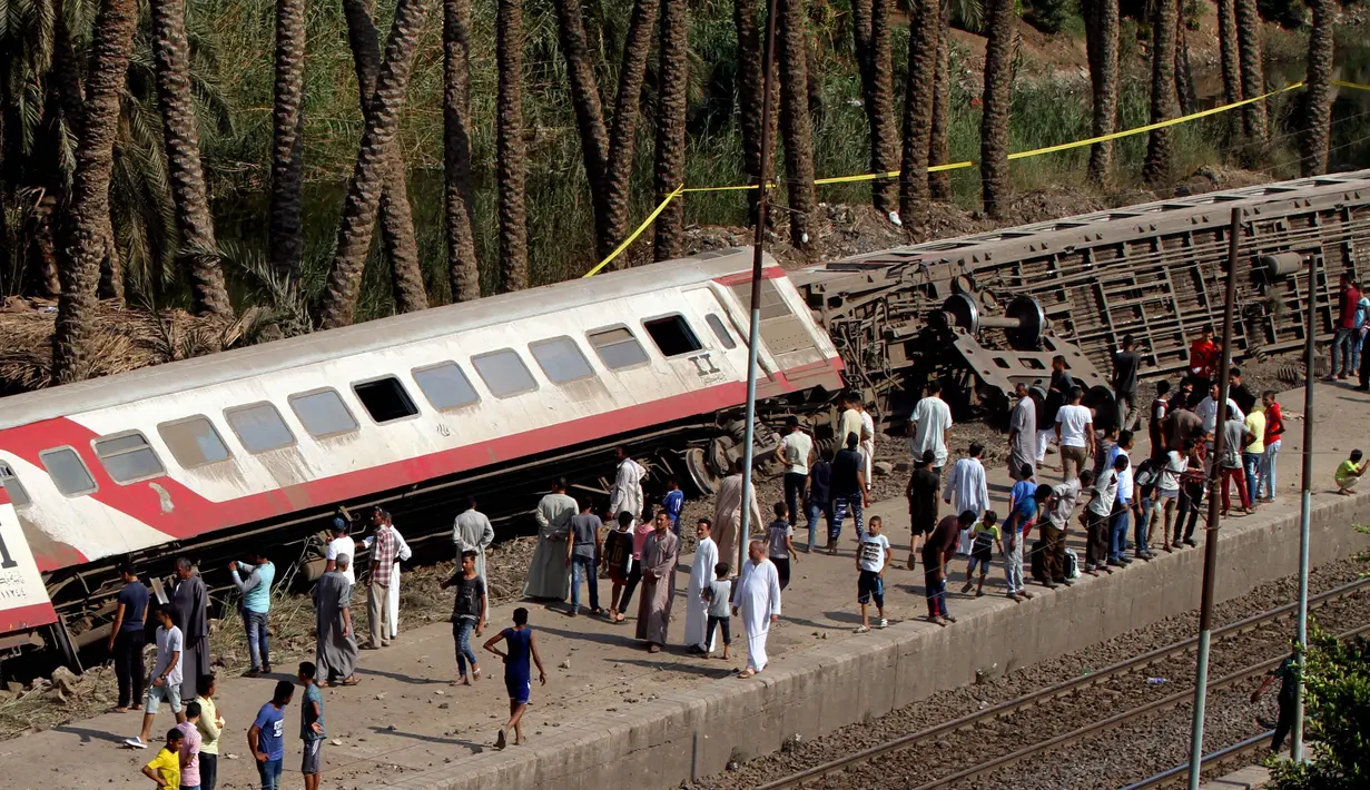 Sejumlah warga melihat gerbong kereta penumpang usai tergelincir saat melintasi jalur di daerah al-Badrasheen, Giza, Mesir, (13/7). Dalam kejadian tersebut, tidak ada korban jiwa dan sekitar 55 penumpang terluka. (AFP Photo/Stringer)