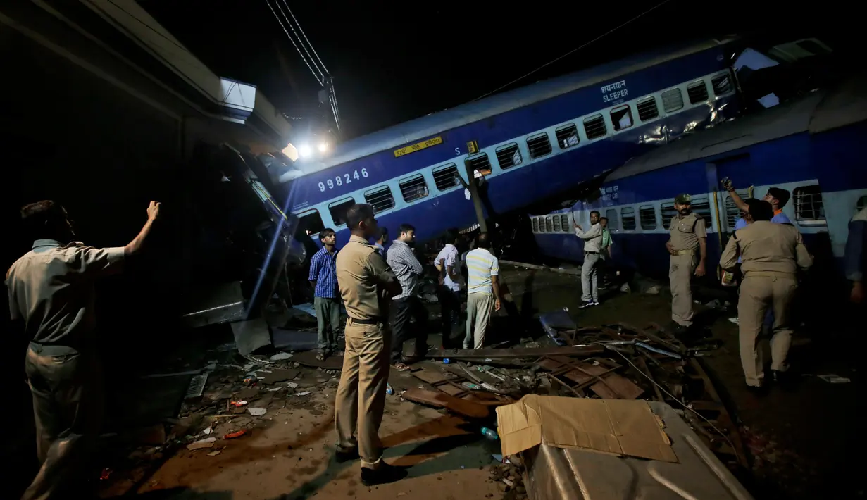 Aparat kepolisian India berdiri dekat gerbong kereta Kalinga-Utkal Express yang tergelincir hingga keluar jalur di Negara Bagian Uttar Pradesh, Minggu (20/8). Beberapa gerbong yang tergelincir menghantam rumah-rumah di dekatnya. (AP/Altaf Qadri)