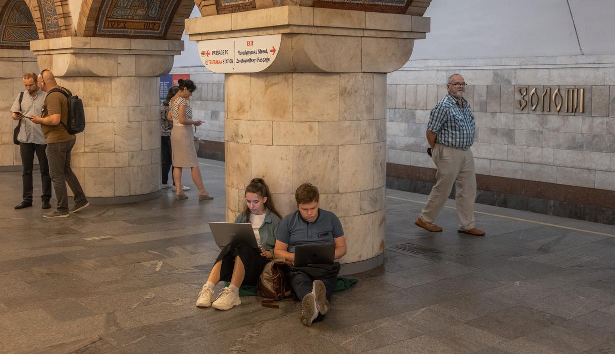 Orang-orang bekerja dengan komputer laptop mereka di stasiun metro saat mereka berlindung di stasiun metro Teatralna selama alarm serangan udara di ibu kota Ukraina, Kyiv, pada 26 Juli 2023, di tengah invasi Rusia ke Ukraina. (Roman PILIPEY / AFP)