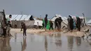 Para pengungsi terpaksa menggali parit secara manual di sekitar tenda untuk mengalirkan air. Tampak dalam foto, warga Palestina berjalan melewati area yang tergenang banjir di kamp tenda sementara setelah hujan lebat di Kota Gaza, Kamis, 26 Maret 2026 (AP Photo/Jehad Alshrafi)