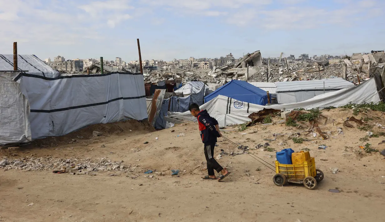 Dalam tugasnya, NCAG akan bertanggung jawab kepada Dewan Perdamaian Gaza. Tampak dalam foto, seorang anak laki-laki Palestina yang mengungsi dan hidup di antara reruntuhan rumah dan bangunan yang hancur akibat serangan militer Israel selama lebih dari dua tahun di wilayah Gaza, menyeret kontainer berisi air di kamp pengungsi Jabalia, di bagian utara Jalur Gaza pada Sabtu 17 Januari 2026. (Omar AL-QATTAA/AFP)