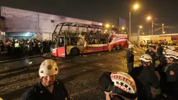 Petugas kepolisian berdiri dekat kerangka  bus bertingkat yang hangus terbakar di terminal bus antarprovinsi, kota Lima, Peru, Minggu (31/3). Pihak berwenang masih menyelidiki penyebab pasti mengapa bus yang penuh penumpang itu ludes dilalap api. (Photo by Luka GONZALES / AFP)