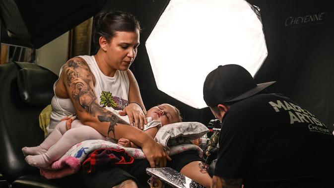 Seorang wanita membawa bayinya saat menato kakinya selama Expotattoo Colombia 2019 di Medellin, departemen Antioquia (2/6/2019). Para penggila tato antusias untuk mentato tubuhnya di festival tato terbesar di negara tersebut. (AFP Photo/Joaquim Sarmiento)