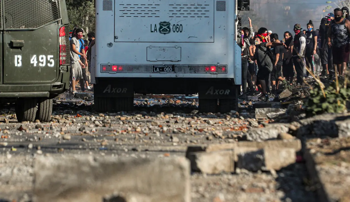 Demonstran melempar batu saat bentrok dengan polisi di lingkungan miskin di Santiago, Chili, (18/5/2020). Presiden Chile, Sebastián Piñera berjanji bahwa pemerintahnya akan menyediakan lagi 2,5 juta paket makanan dan kebutuhan pokok lainnya sekitar satu minggu ke depan. (AP Photo/Esteban Felix)