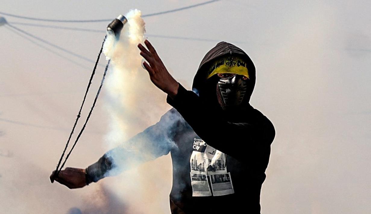 Seorang pemuda Palestina menggunakan ketapel untuk mengembalikan tabung gas air mata ke arah pasukan keamanan Israel saat bentrok pada demonstrasi menentang pengambilalihan tanah oleh Israel dekat pemukiman Yahudi Kedumim di Desa Kfar Qaddum, Tepi Barat, 21 Januari 2022. (JAAFAR ASHTIYEH/AFP)