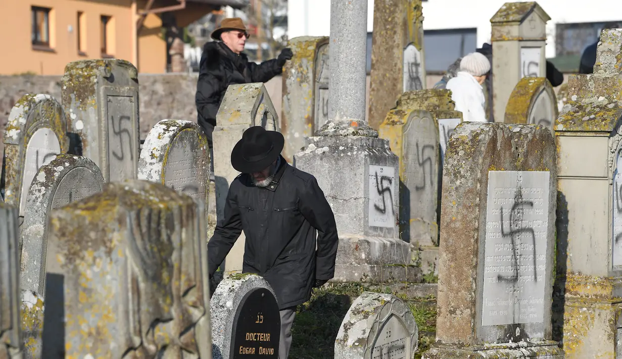 Orang-orang melihat makam yang dicoreti lambang swastika Nazi di pemakaman Yahudi, Westhoffen, dekat Strasbourg, Prancis, Rabu (4/12). Sedikitnya 107 makam menjadi sasaran vandalisme dengan dicoreti lambang swastika Nazi. (AFP/Patrick Hertzog)