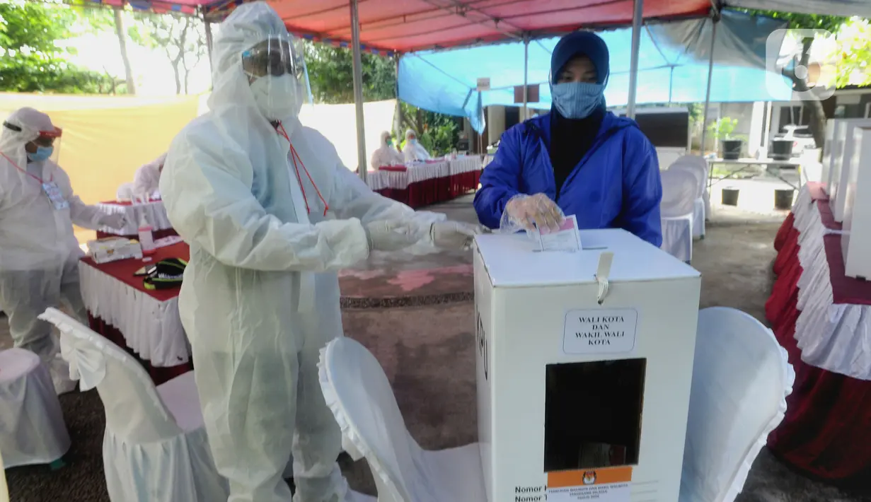 Petugas Kelompok Penyelenggara Pemungutan Suara (KPPS) dengan memakai baju hazmat membantu pemilih memasukkan kertas suara usai menggunakan hak pilihnya dalam Pilkada Tangerang Selatan 2020 di TPS 46, Paku Jaya, Serpong Utara, Rabu (9/12/2020). (merdeka.com/Arie Basuki)