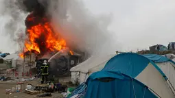 Petugas memadamkan kobaran api di pengungsian imigran "Jungle", di kota pelabuhan Calais, Prancis (26/10). Karena kumuh pemerintah Prancis akhirnya mulai mengosongkan kamp pengungsian imigran tersebut. (REUTERS/Philippe Wojazer)