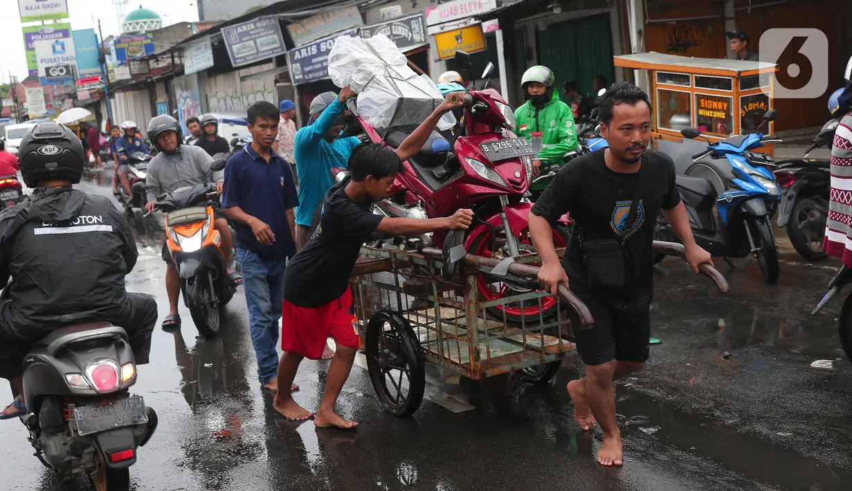 Warga mengangkut sepeda motor menggunakan gerobak melintasi banjir di jalan KH Hasyim Ashari, Kota Tangerang, Banten, Sabtu (16/7/2022). Warga sekitar membantu para pengendara yang melintas agar tidak terkena banjir dengan menawarkan jasa gerobak. (Liputan6.com/Angga Yuniar)