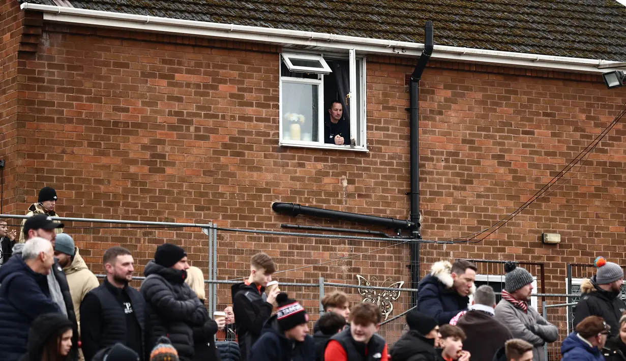 Seorang warga menonton dari jendela pada laga Piala FA 2024/2025 antara Tamworth melawan Tottenham Hotspur di The Lamb Ground, Tamworth, Inggris, Minggu (12/01/2025) waktu setempat. (AFP/Henry Nicholls)