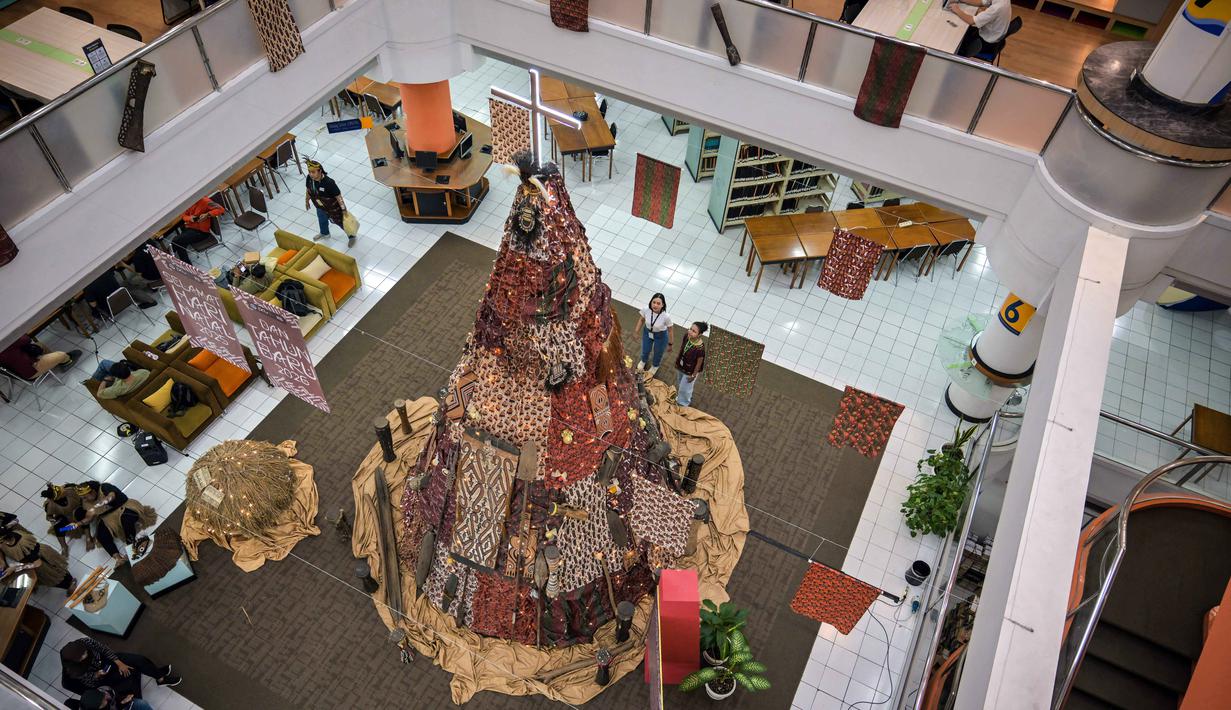 Salah satu mahasiswa berdiri di samping instalasi dekorasi berbentuk pohon Natal dengan motif budaya Papua di Perpustakaan Petra Christian University (PCU), Surabaya, Jawa Timur, Kamis 18 Desember 2025. Jelang perayaan Natal 2025, perpustakaan Petra Christian University (PCU) kembali menghadirkan instalasi dekorasi Pohon Natal tematik. (JUNI KRISWANTO/AFP)