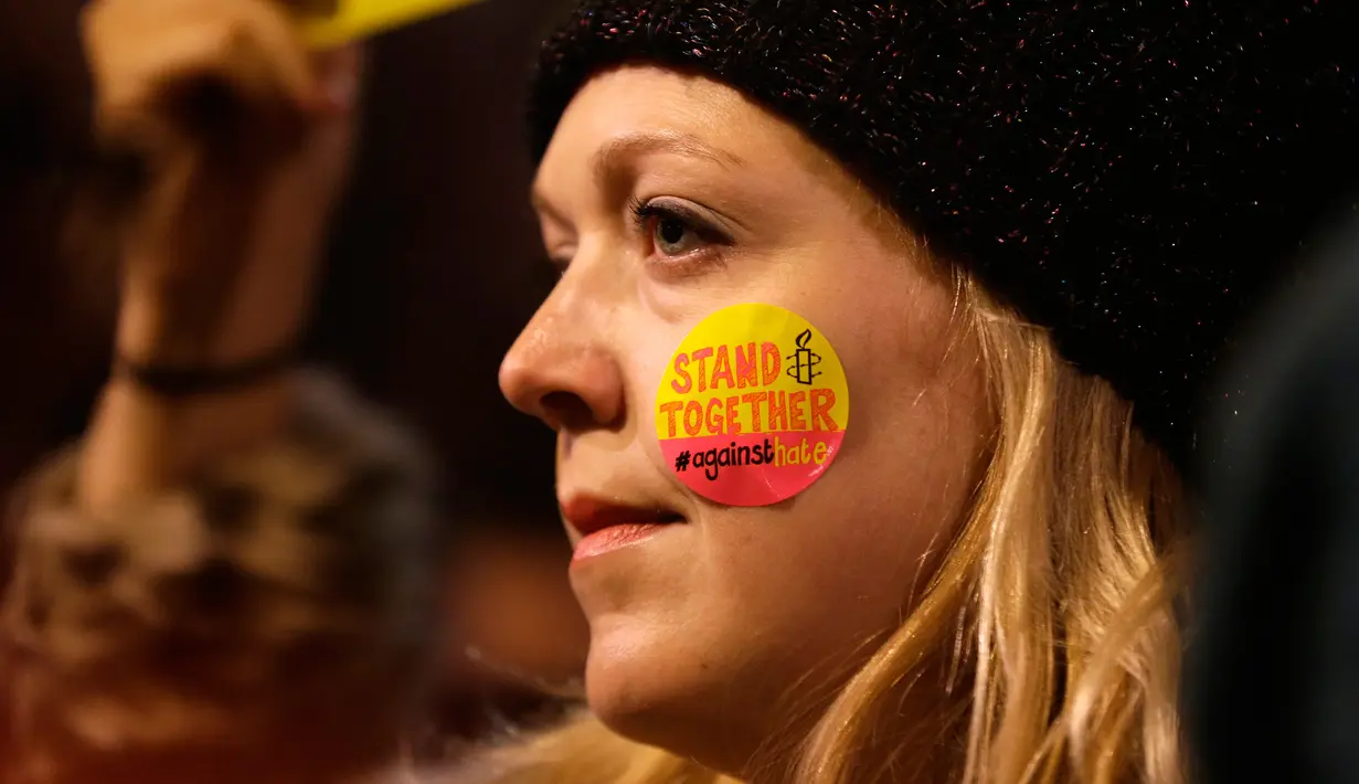 Seorang wanita menempelkan stiker ke pipinya dalam unjuk rasa di luar Downing Street, London, Senin (30/1). Ratusan orang di London turun ke jalan menentang kebijakan Presiden AS Donald Trump menyangkut kependudukan dan imigrasi. (AP Photo/Alastair Grant)