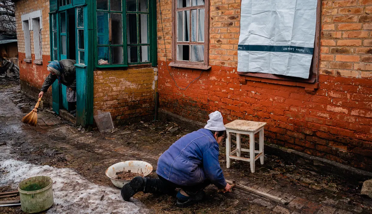 Seorang wanita berusaha menutupi jendela yang pecah dengan menempelkan selembar plastik setelah penembakan di Chasiv Yar, dekat Bakhmut pada 28 Februari 2023. Militer Ukraina mengatakan pada hari Selasa, Rusia menggempur permukiman di sekitar Bakhmut yang memiliki populasi sebelum perang sekitar 70.000 orang, namun kini menjadi reruntuhan. (Dimitar DILKOFF/AFP)