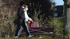 Orang-orang berjalan melewati bangku yang dipasangi garis polisi di Brussel, Belgia, pada 25 Maret 2020. Deretan bangku di sejumlah taman dilarang diduduki untuk mencegah orang-orang berkumpul atau berada terlalu lama di area publik tersebut. (Xinhua/Zheng Huansong)