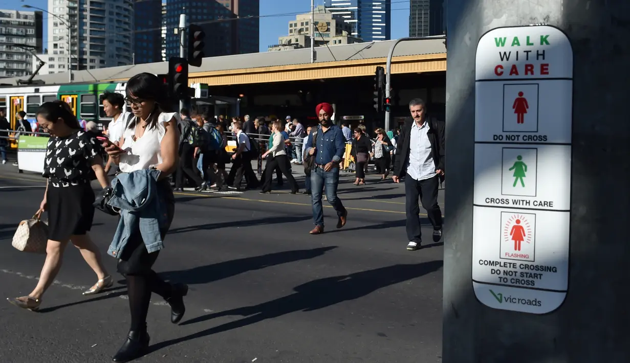 Warga melintasi penyebrangan dekat Petunjuk sinyal lalu lintas untuk pejalan kaki yang baru ditampilkan pada tiang dekat Stasiun Flinders Street pada Hari Perempuan Internasional di Melbourne, Australia, Rabu (8/3). (AFP Photo / Paul Crock)