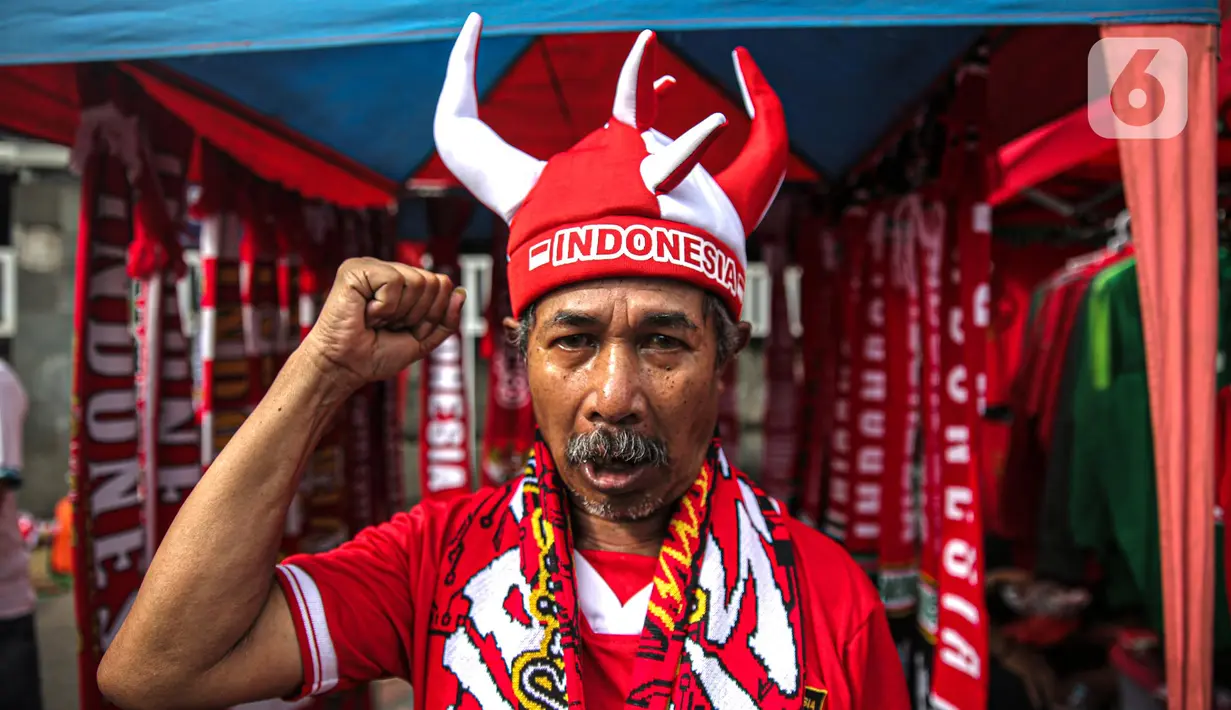 Pedagang mengenakan atribut timnas Indonesia jelang pertandingan AFF 2022 antara Indonesia melawan Thailand di Stadion Gelora Bung Karno, Jakarta, Kamis (29/12/2022). Atribut timnas Indonesia seperti kaos, syal, dan topi dijual dengan kisaran harga Rp35.000 hingga Rp75.000. (Liputan6.com/Faizal Fanani)