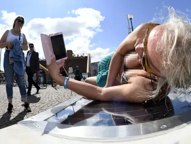 Lena Salmi mengisi baterai ponselnya saat berjemur di bangku panel surya di Helsinki, Finlandia, (9/7). Bangku panel surya dapat digunakan untuk mengisi ulang sepeda listrik dan perangkat mobile. (AFP Photo/Lehtikuva/Martti Kainulainen)