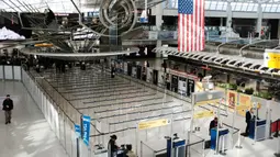 Orang-orang berjalan melalui terminal keberangkatan internasional yang sepi di Bandara John F. Kennedy (JFK), New York City, Sabtu (8/3/2020). Maskapai penerbangan terpukul wabah virus corona (COVID-19) setelah pelancong bisnis maupun rekreasi membatalkan rencana. (Spencer Platt/Getty Images/AFP)