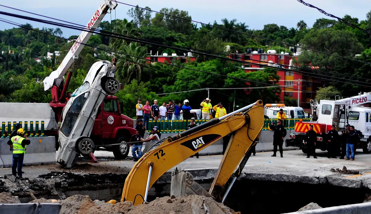 Tim penyelamat menggunakan derek untuk mengangkat sebuah mobil yang tertelan ke dasar lubang di jalan raya Meksiko-Cuenava, Meksiko, Rabu (12/7). Lubang yang tiba-tiba muncul itu membunuh seorang ayah dan putranya yang tengah berkendara. (AP/Tony Rivera)
