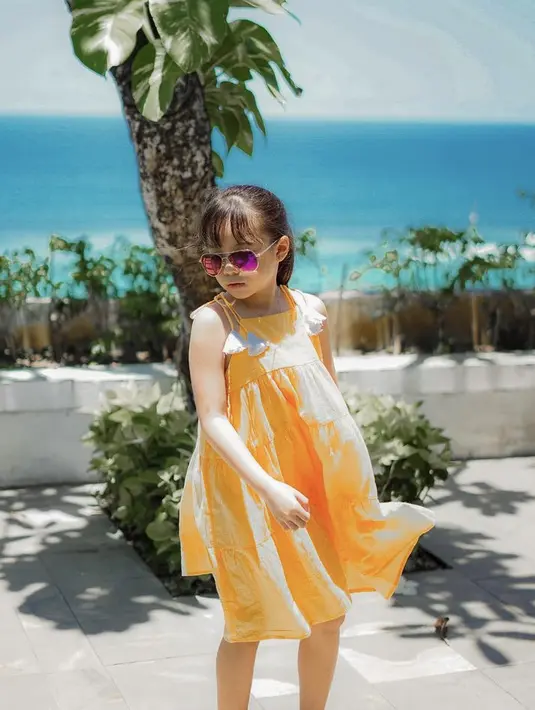 Gempita tampil menggemaskan dengan dress orange, ia pun bergaya mengenakan kacamatanya. Rambut panjangnya pun diikat ke belakang.  Credit: Instagram/(@gisel_la)