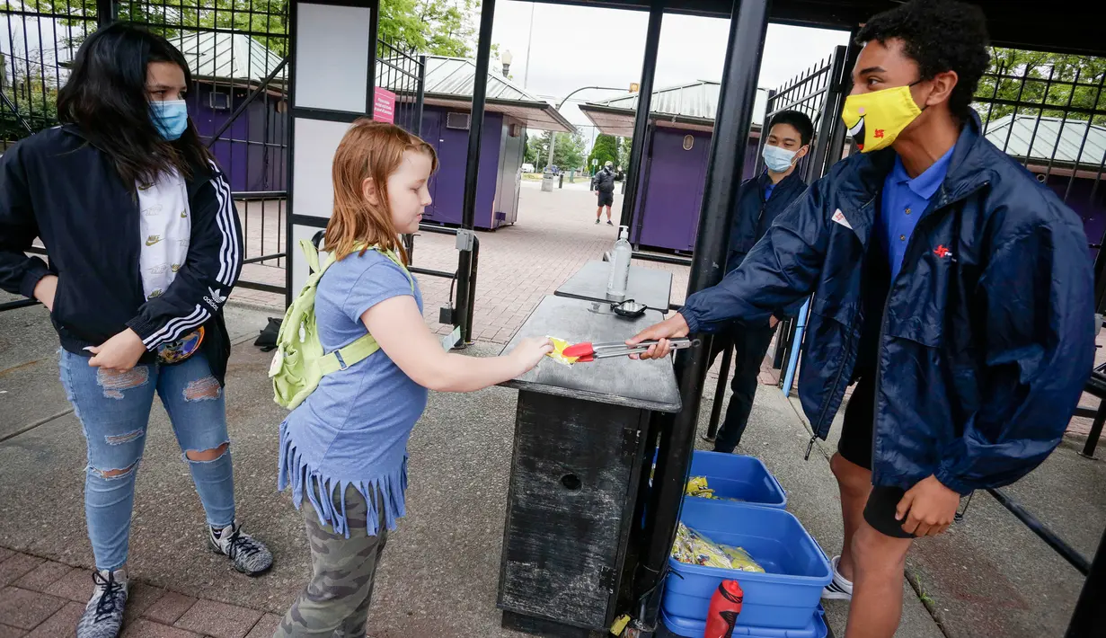 Petugas membagikan masker gratis kepada pengunjung di pintu masuk Playland Amusement Park, di Vancouver, British Columbia, Kanada, pada 10 Juli 2020. Playland Amusement Park dibuka kembali untuk umum pada Jumat (10/7), dengan langkah-langkah protokol kesehatan. (Xihua/Liang Sen)