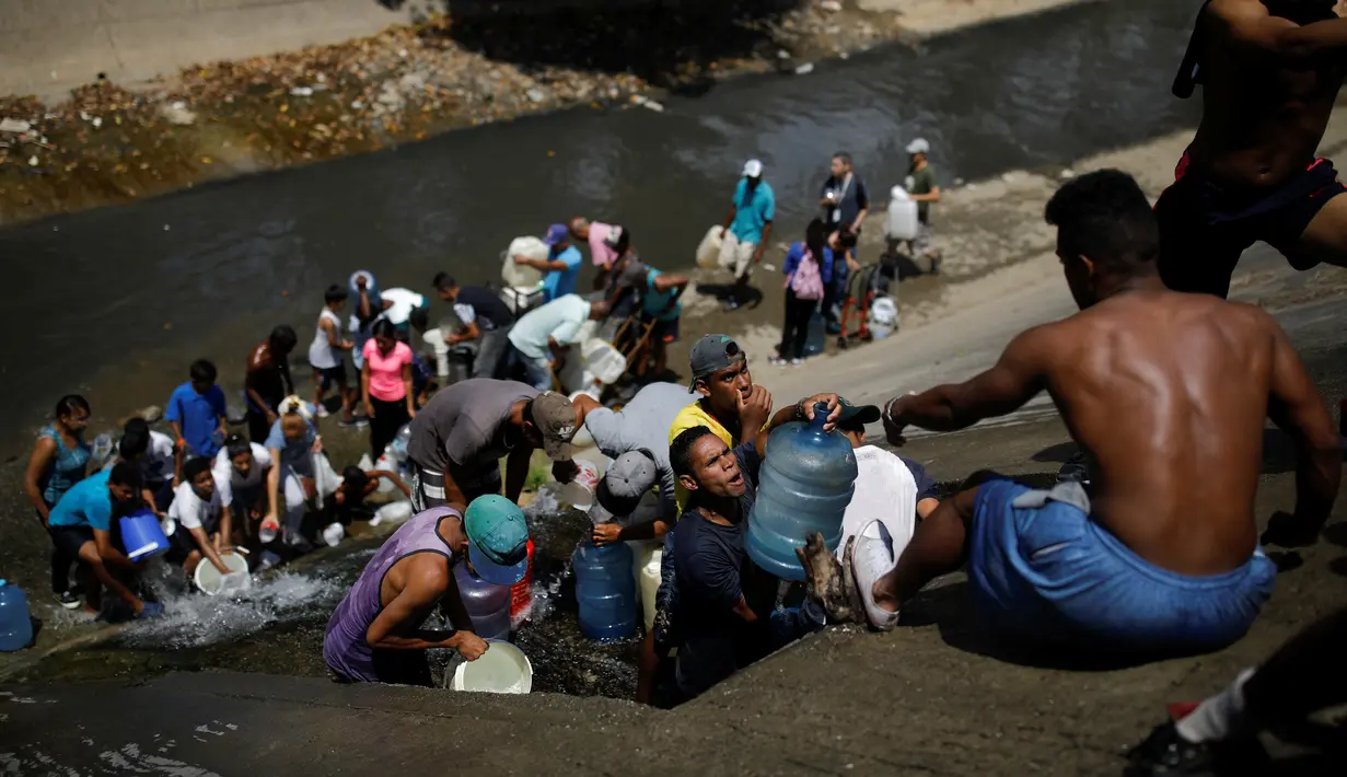Orang-orang mengumpulkan air yang keluar melalui saluran pembuangan air limbah yang mengalir ke Sungai Guaire di Caracas, 11 Maret 2019. Pemadaman listrik selama berhari-hari di Venezuela berdampak terhadap krisis air. (REUTERS/Carlos Garcia Rawlins)